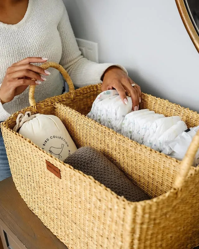 Person holding a woven basket with folded clothes inside, on a wooden surface.