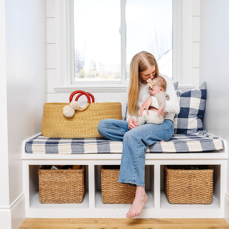 Woman sitting on a bench with a child, surrounded by storage baskets and a plaid pillow.