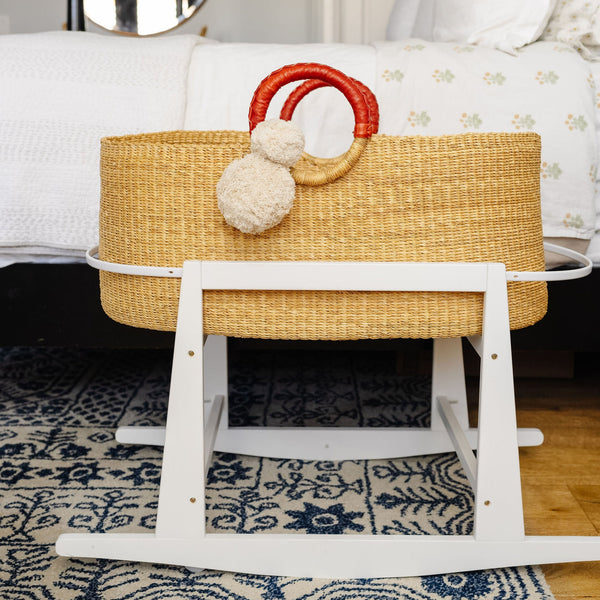 Wicker Moses basket with white stand on a patterned rug in a room.