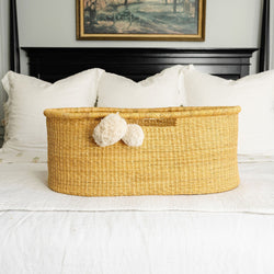 Wicker basket with decorative pom-poms on a bed in a bedroom setting.